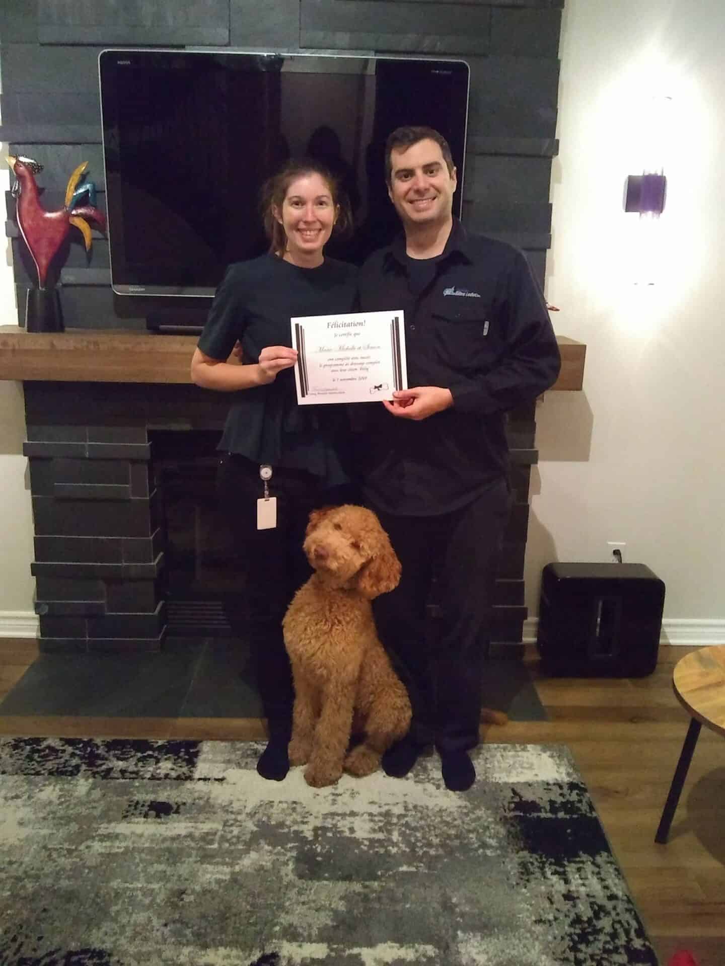 Deux personnes avec leur chien à leur pieds, tenant un certificat de dressage de chien.