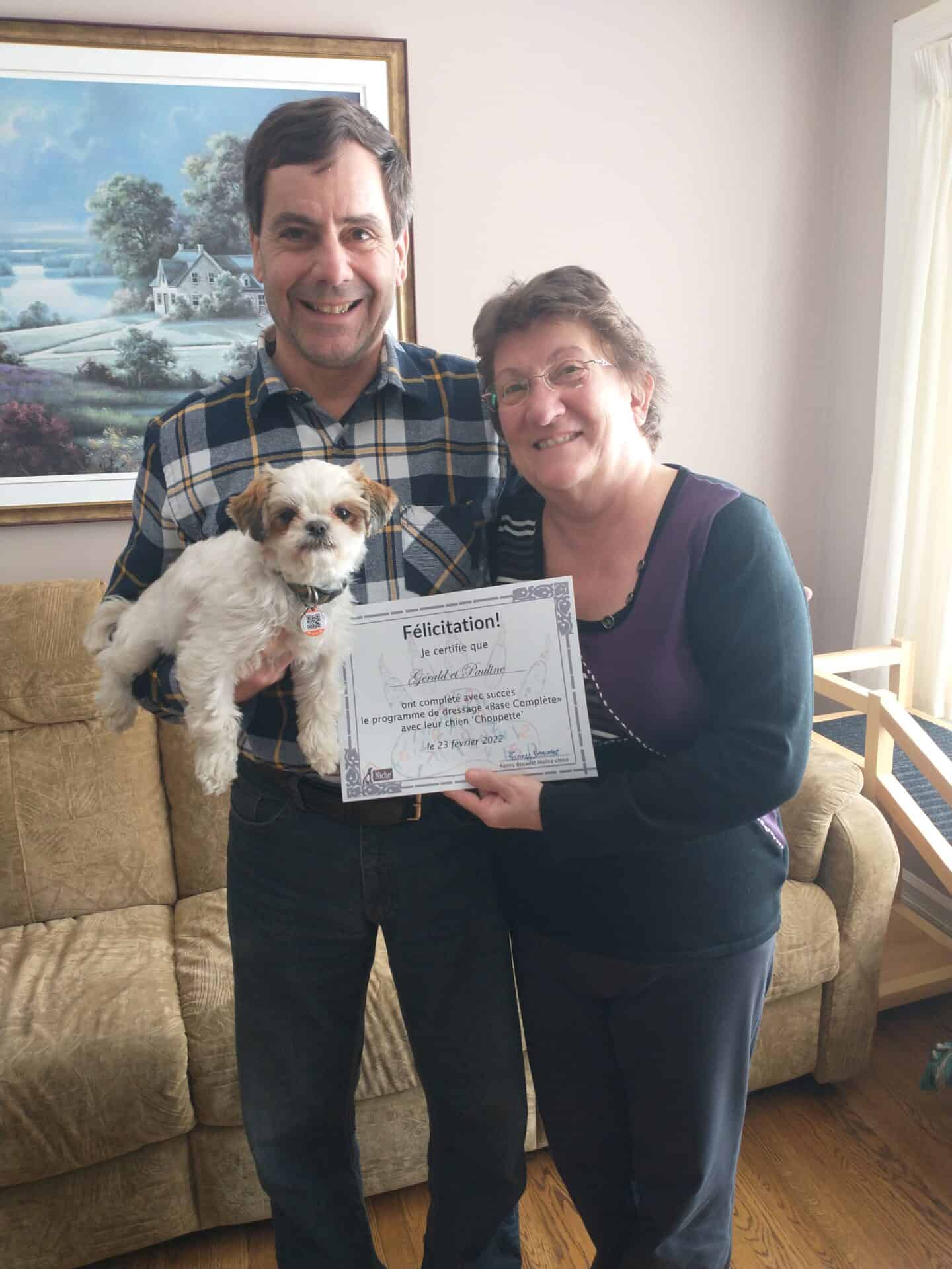 Deux personnes tenant un chien et un certificat de dressage de chien.
