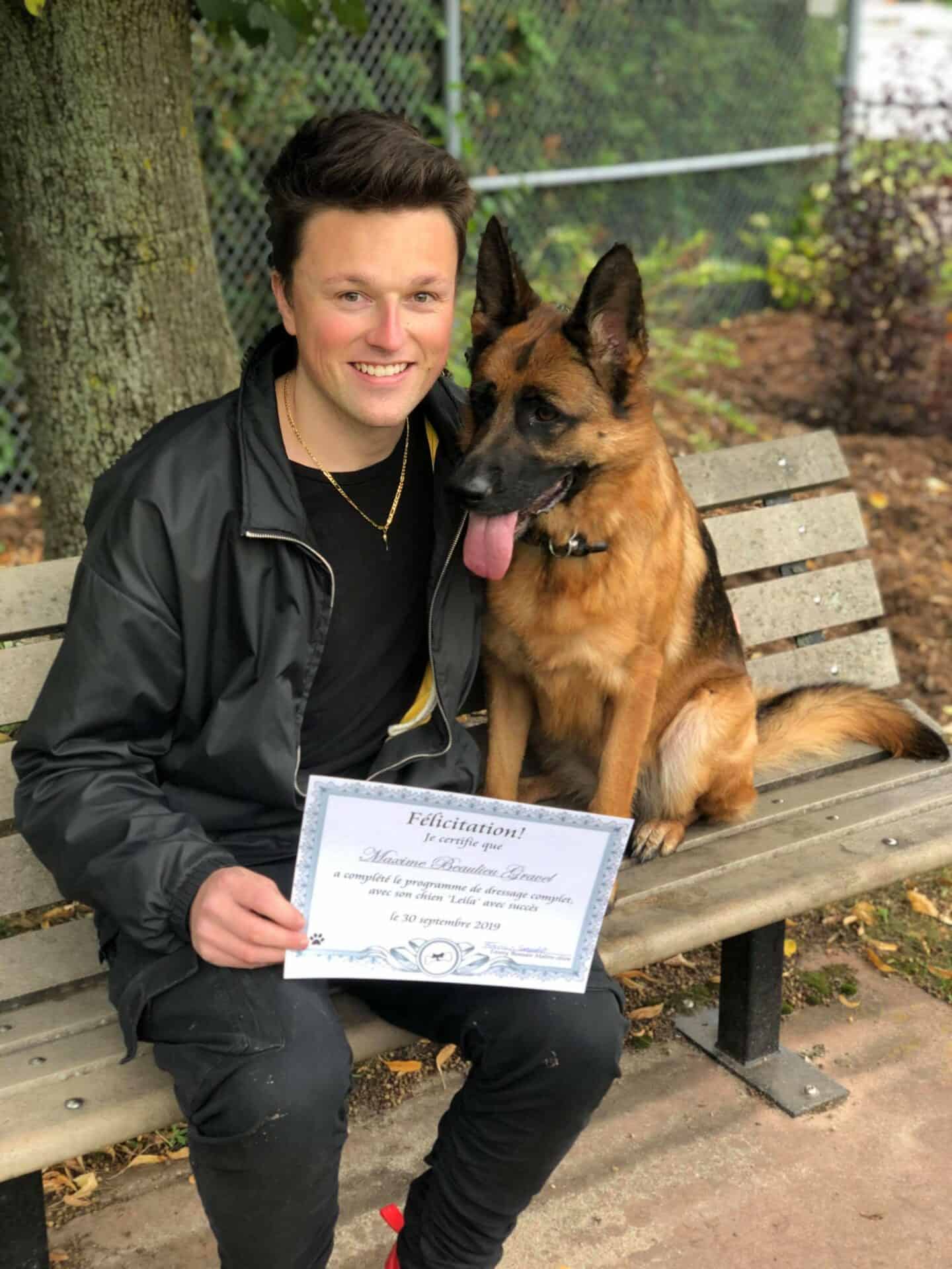 Chien avec son maître assis sur un banc, le maître tenant le certificat de dressage canin que son chien a obtenu.